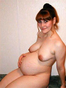 Pregnant redhead takes off her seductive red lingerie and poses naked on a bed